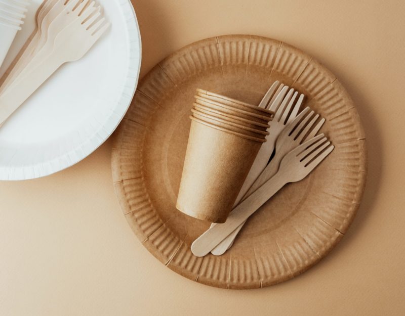 Brown and white disposable paper cups and wooden forks on beige background