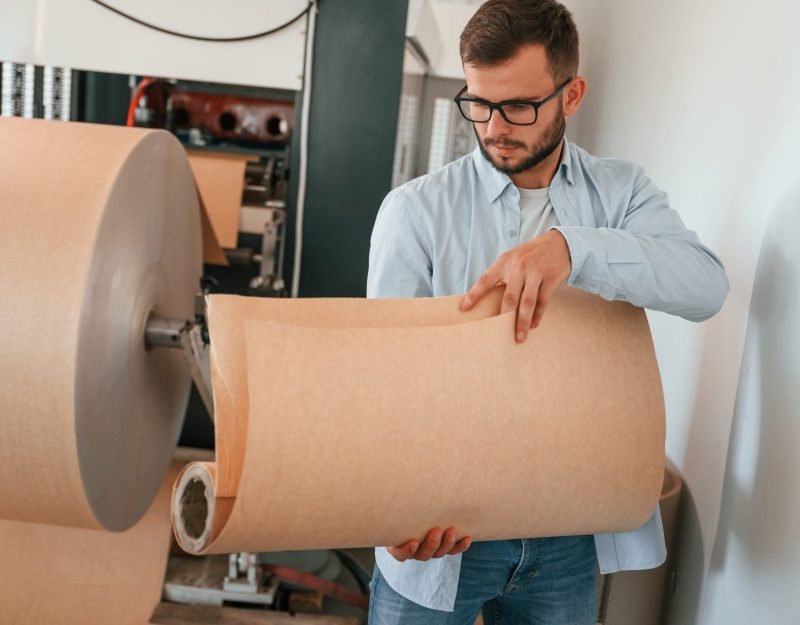 Holding pieces of wooden sheets. Print house worker in white clothes is indoors.